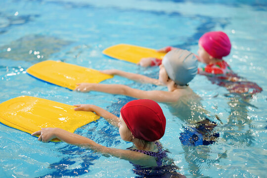Little kids swimming with kickboards during lesson in pool, selective focus