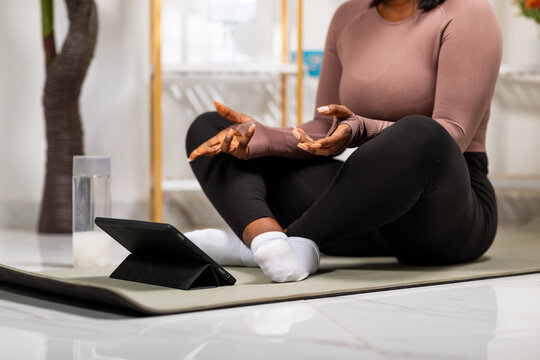 African woman meditating on a yoga mat using a tablet for an online wellness session