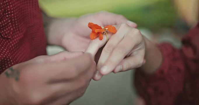 A man placing a flower ring on a finger, a woman accepts a love proposal, a romantic outdoor scene of a symbolic ring, bonding, and emotional connection