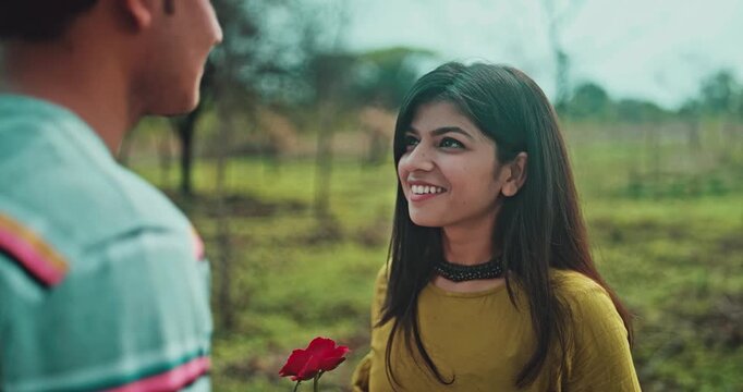 A young couple's love proposal in a park with red rose, joyful acceptance, an emotional relationship scene of asking and accepting love with a smile and blush