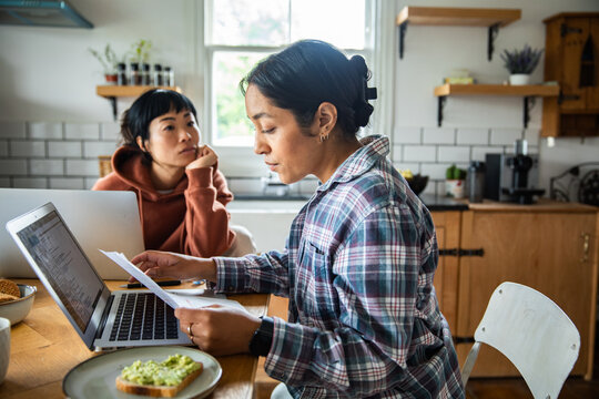 Two women reviewing household bills on laptop at home kitchen table