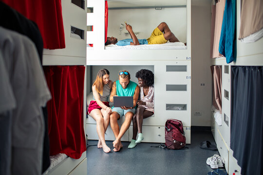 Young travelers using laptop in modern hostel dormitory