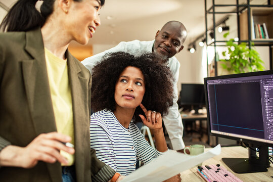 Diverse coworkers discussing design project at computer in modern office