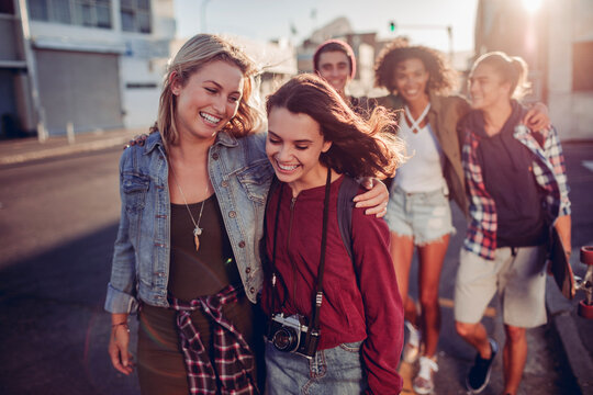 Young friends walking and laughing on a city street at sunset