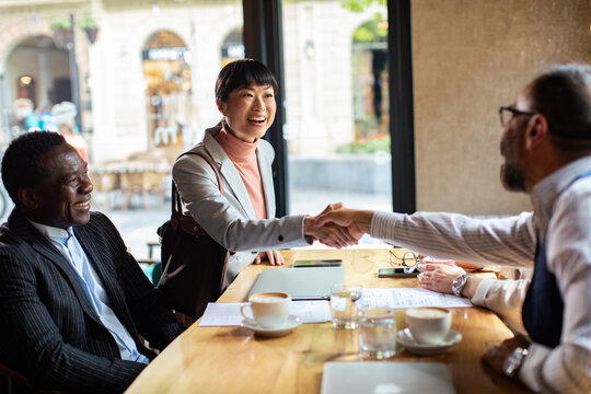 Business professionals shake hands at cafe meeting