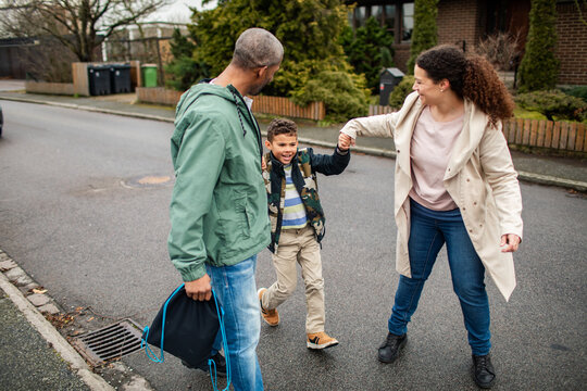 Parents swing son while walking on suburban street