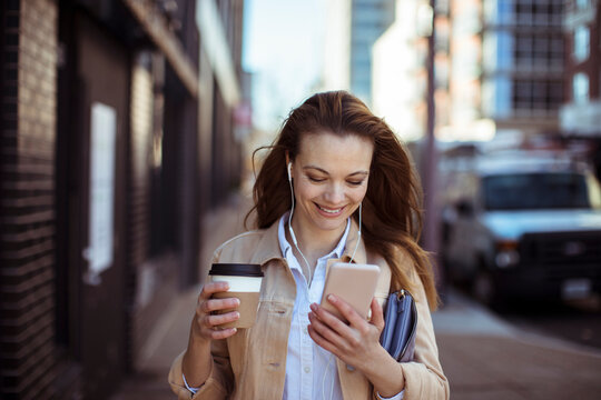 Smiling young woman with coffee and smartphone on city street