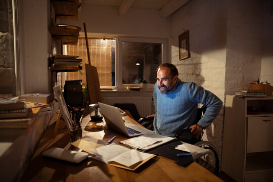 Smiling man in wheelchair working late at home office