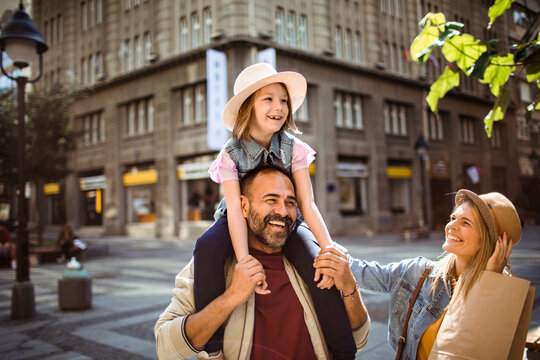 Smiling parents carry daughter on sunny city street
