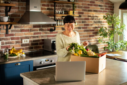 Smiling woman unboxing vegetable delivery box in home kitchen