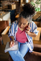 Naklejka premium Middle-aged woman on phone taking notes while planning move at home