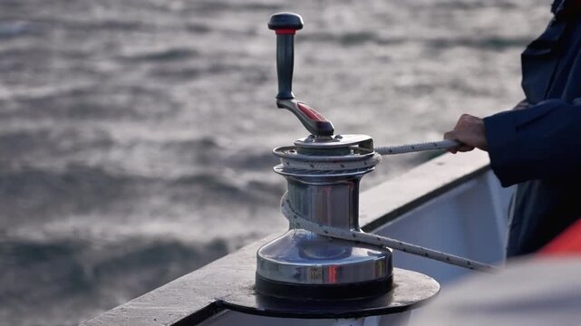 sailor tightening rope on winch aboard sailboat