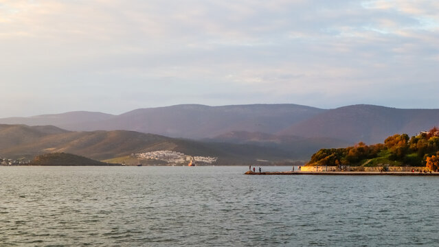 Gulluk bay seascape with people fishing on a pier, coastal town and mountains in Milas, Turkey