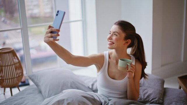 Sensual woman posing mobile phone selfie in morning bed closeup. Modern female