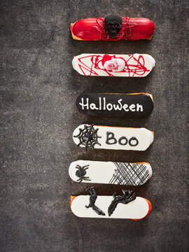 Six Halloween-themed eclairs are decorated with various spooky designs including skulls and cobwebs. These festive desserts are ideal for seasonal events, bakery promotions, or Halloween parties