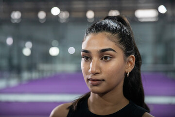 Adult Indian woman looking left in arena wearing black top, hoop earrings, purple court, copy space © wavebreak3