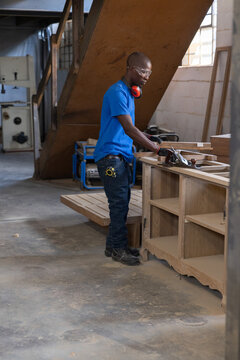 Woodworker using hand planer on wooden cabinet frame on sturdy workbench in carpentry workshop