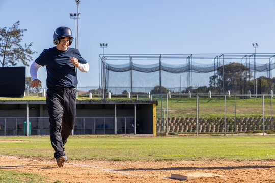 Mature male running toward home plate on ballfield wearing batting helmet navy shirt, copy space