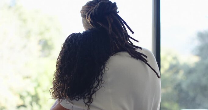 African American couple hugging at window, man loosening hug, talking, touching jaw, wrist bracelet