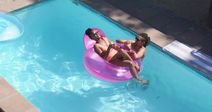 Two women arriving floating on pink float in home pool, passing drink, socializing, copy space