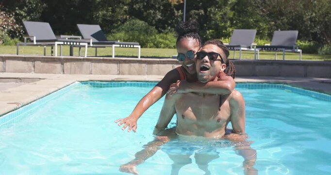 Couple starting from piggyback while playing, woman reaching outward, man paddling forward in pool