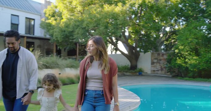Diverse family walking stepping off pool border onto grassy lawn holding hands for family time
