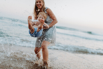 Plakat Mother playing with little son in shallow sea water during family beach vacation.