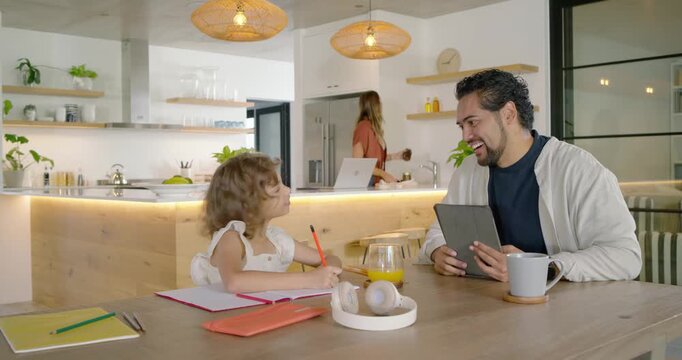 Family girl asking feedback drawing red pencil at kitchen table dad using tablet mom getting bottle