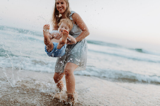 Mother playing with little son in shallow sea water during family beach vacation.