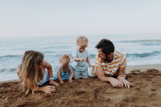 Two toddler children playing on sand beach with paretns during summer holiday.