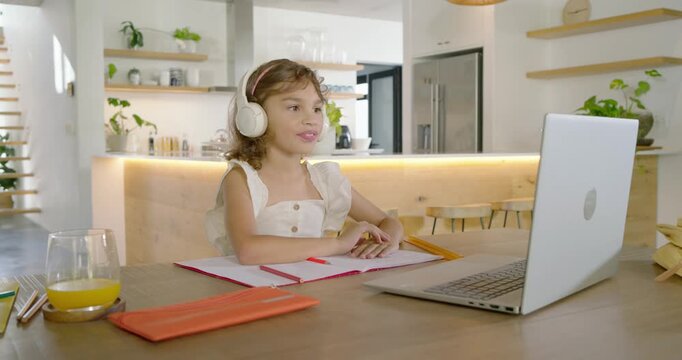 African American child replying to lesson on laptop at home adjusting headset, writing red notebook