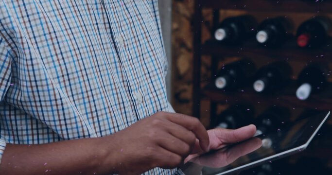 Tapping mid adult man using tablet at wine shop, with checked-shirt, wooden wine rack and bottles
