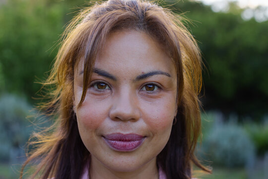 African woman posing closeup in garden backlit wearing light pink collared top, small hoop earring