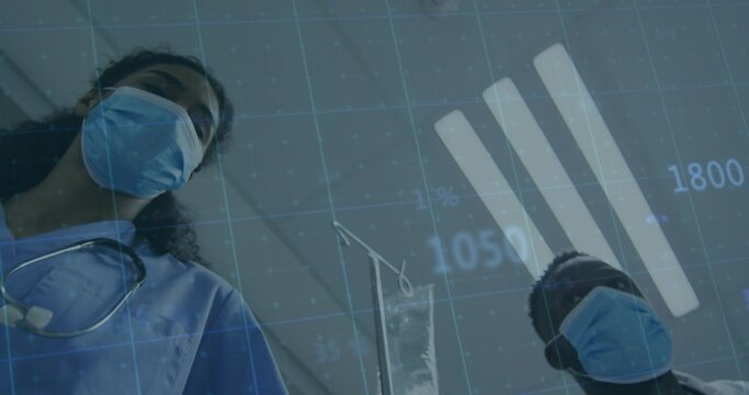 Seeing two staff in blue scrubs wearing masks leaning over patient at clinic bay, IV pole