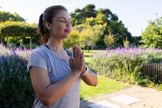 African American woman standing in garden, pressing palms in prayer, wearing gray tee, fitness band