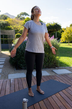 African American woman breathing on wooden deck mat in grey tee, black leggings with bottle nearby