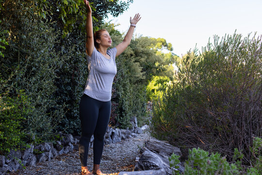 African American adult woman raising arms overhead on gravel trail wearing grey tee and tracker