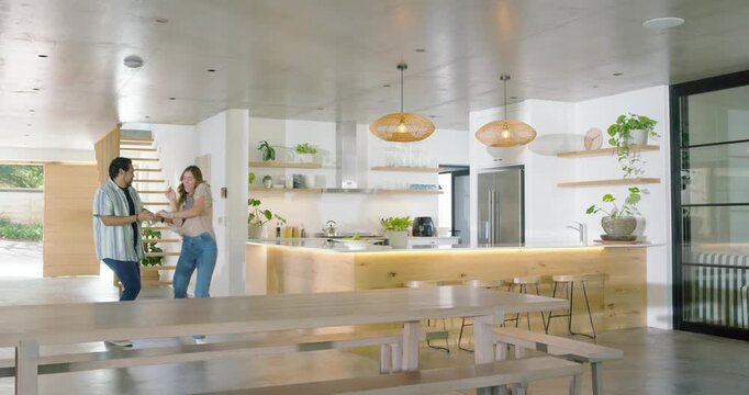 Diverse couple entering kitchen, taking hands and dancing playfully around island, copy space
