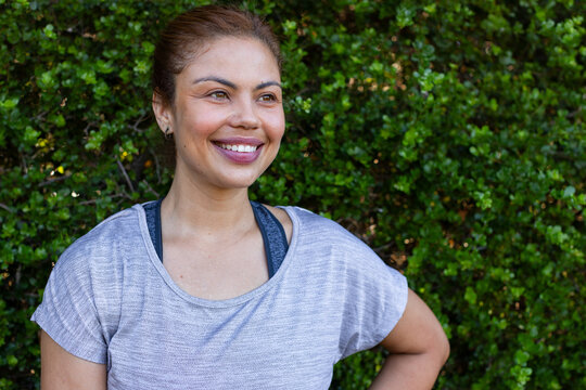 African American woman smiling looking right by hedge wearing gray top dark sports bra stud earring