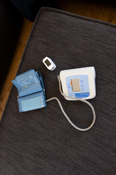 Digital BP monitor and pulse oximeter are resting on gray ottoman, floor edge visible