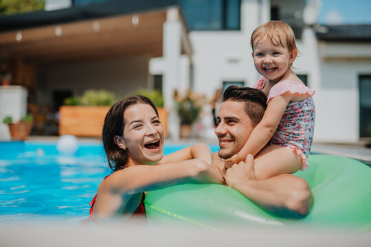 Parents and child having fun with floatie in garden swimming pool