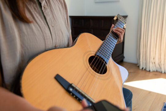 Acoustic guitar is resting across lap in room, with sunlight on hardwood floor and dresser visible