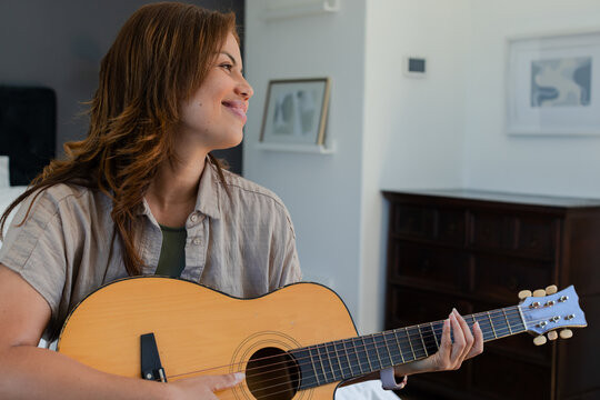 African American woman sitting on bed holding acoustic guitar across lap wearing beige shirt