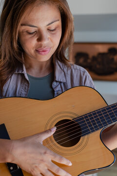 Female guitarist holding acoustic guitar, plucking strings and looking at fretboard at home