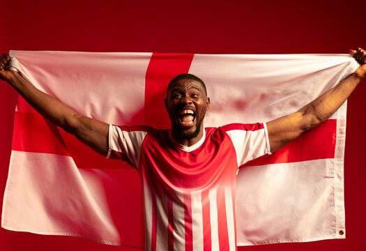 Man in 30s holding white flag with red cross in studio, wearing red-and-white jersey, shouting