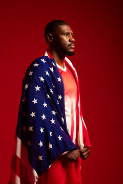 African American man draping American flag on shoulders in red studio wearing jersey-shorts