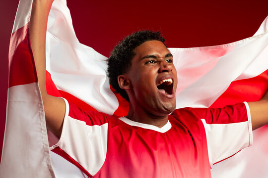 African American man cheering, raising arms and draping red-and-white flag in studio wearing jersey