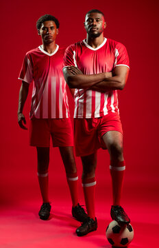 African male soccer players posing in studio wearing red white striped kits and holding soccer ball