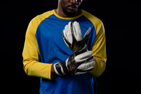 Man adjusting padded goalkeeper gloves while wearing yellow sleeve blue jersey in studio lighting