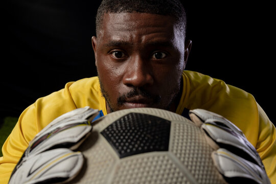 Mid adult male keeper wearing yellow jersey and gloves, holding soccer ball, staring in studio